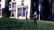 A screenshot of the mannequin-soldier posing by a castle.