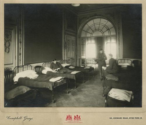 Une photographie en noir et blanc de trois soldats dans une pièce où des lits de camp sont alignés.