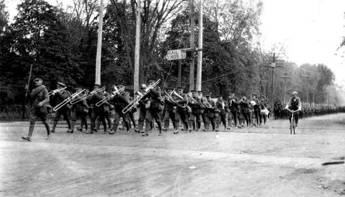 A black and white photograph of a group of soldiers marching, lead by a  military brass band.