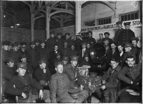 Une photographie en noir et blanc de soldats canadiens assis autour d’un phonographe.