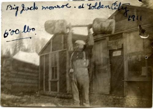 A black and white photograph of Jack Munroe lifting a 600-pound makeshift dumbbell over his head.