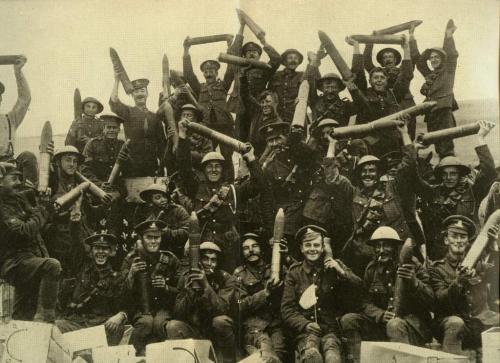 Une image en noir et blanc d’un grand groupe de joyeux soldats canadiens brandissant des obus dans les airs.