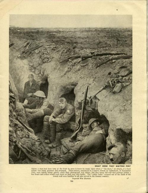 A black-and-white photograph of five soldiers crouched in small holes dug in   the side of a long trench.