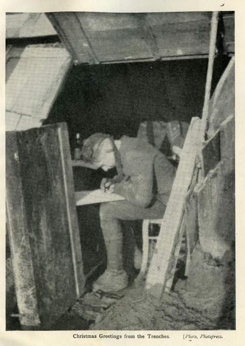 A black-and-white photograph of a soldier sitting inside a trench writing a letter.