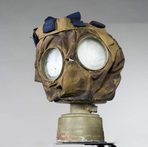 A canvas gas mask with goggle eyes and a small, metal canister on the bottom.