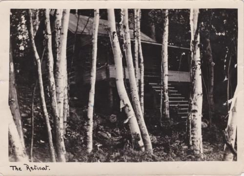 Une photographie en noir et blanc d’un chalet dans les bois.