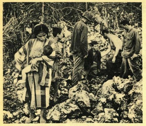 A black-and-white photograph of soldiers with Korean civilians, including a mother and her baby.