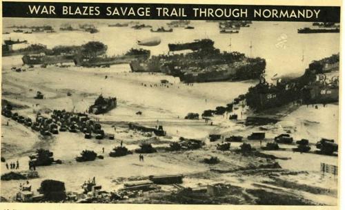 A black-and-white photograph of ships landing on the beach with barrage balloons in the background.