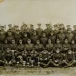 A panoramic black-and-white photograph of soldiers posing with a moose calf and bear cub.