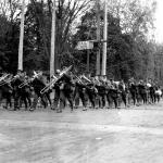 A black and white photograph of a group of soldiers marching, lead by a  military brass band.