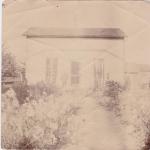 A photograph of a farmhouse with four people outside.