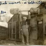 A black and white photograph of Jack Munroe lifting a 600-pound makeshift dumbbell over his head.