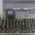 Une photographie en noir et blanc d’un grand groupe de soldats posant  l’extérieur d’une station de recrutement.