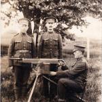 A photograph of two soldiers standing at attention behind a machine gun  manned by a sitting soldier.