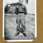 Une photographie en noir et blanc d’un soldat en uniforme posant  devant une maison.