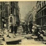 A black-and-white photograph of a civilian and several soldiers in a bombed-out city.